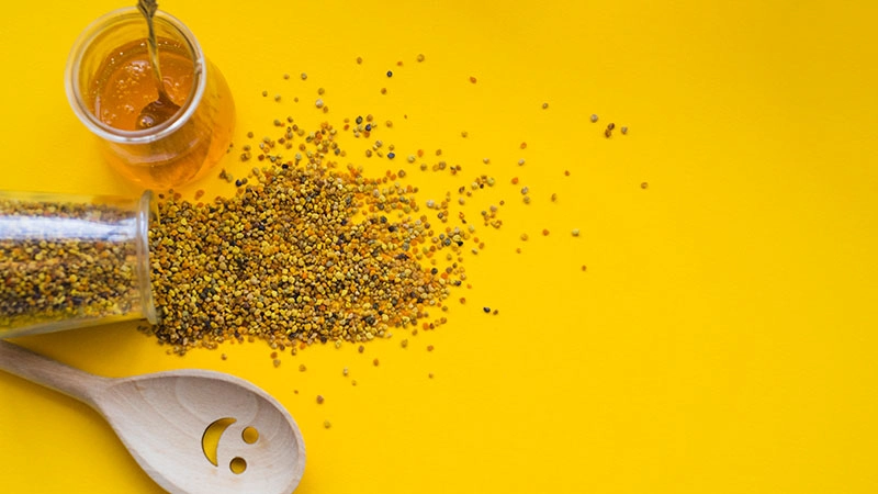 overhead view spilled bee pollens honey pot smiley wooden spoon yellow backdrop